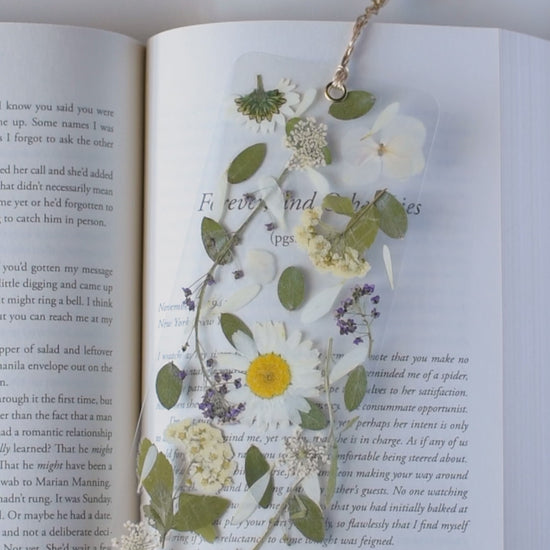 Video de separador de libros transparente con flores prensadas en su interior de color blanco y morado. 