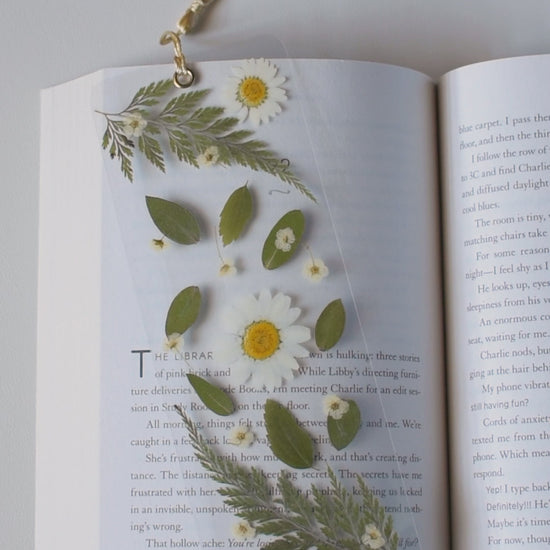 Video de separador de libros transparente con flores prensadas en su interior de color blanco y hojas verdes.