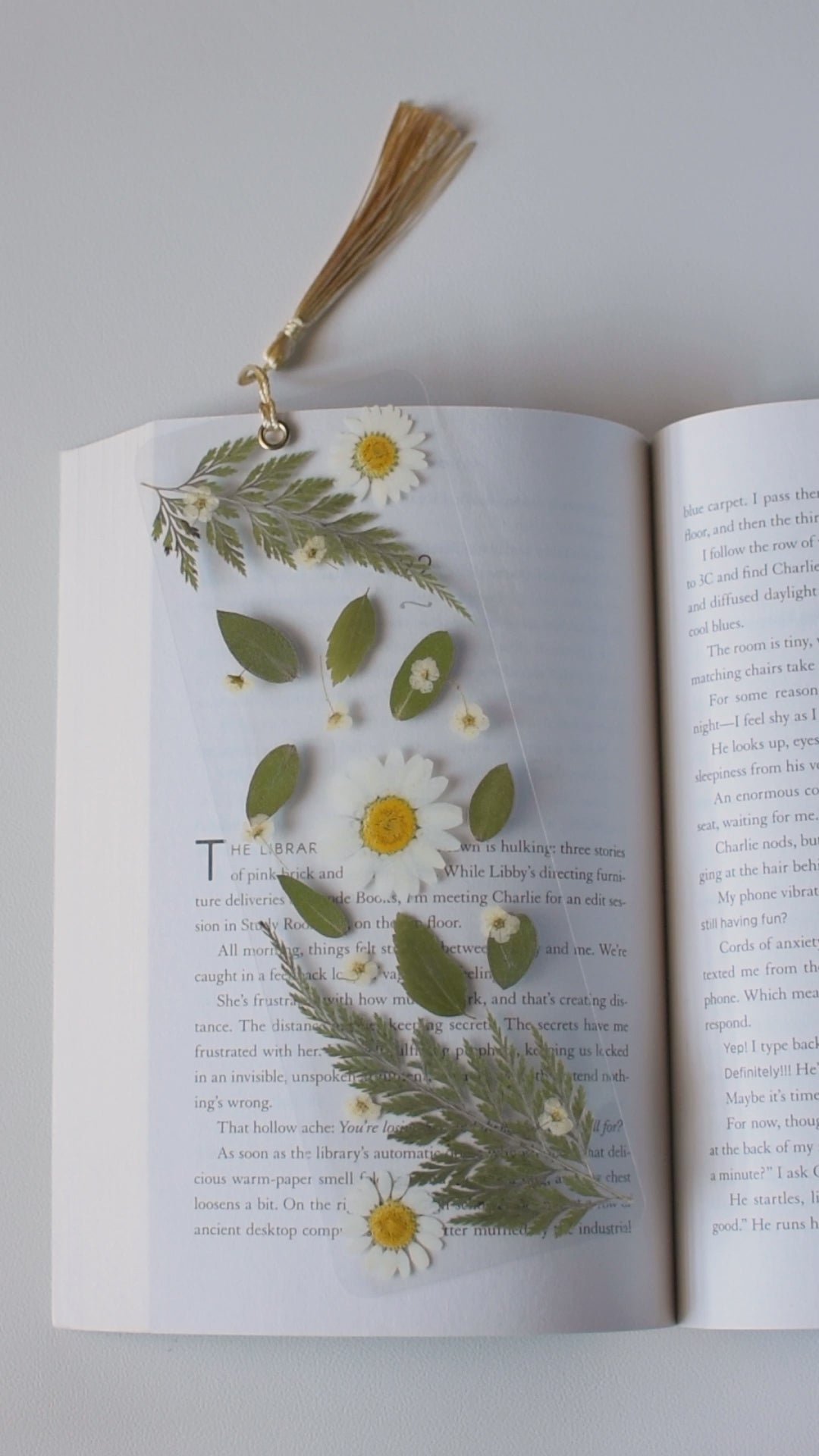 Video de separador de libros transparente con flores prensadas en su interior de color blanco y hojas verdes.