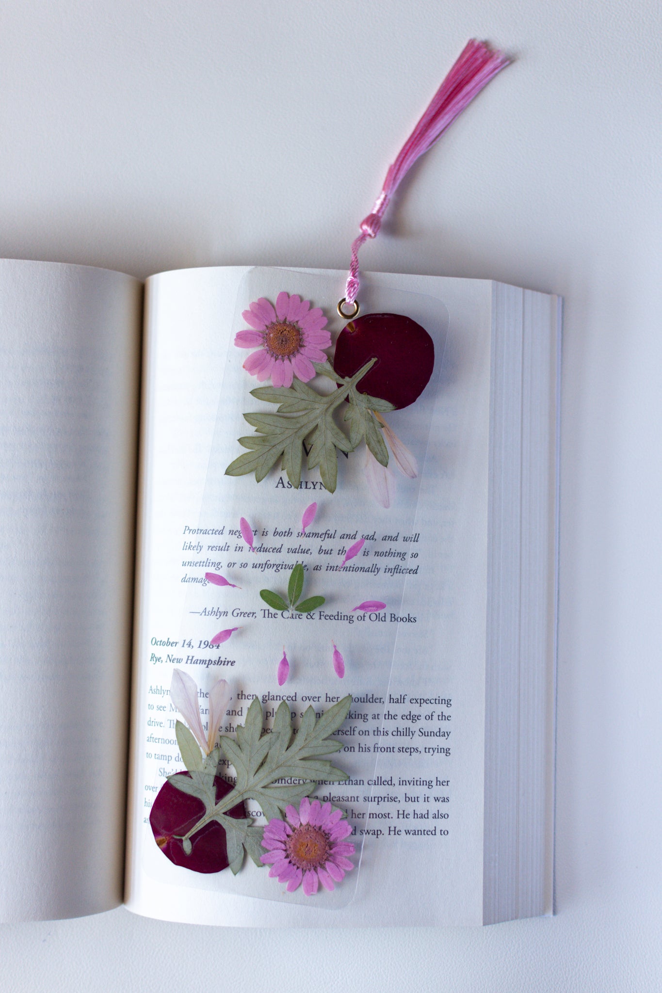 Un separador de libros transparente con flores prensadas en su interior de color rosa y verde.