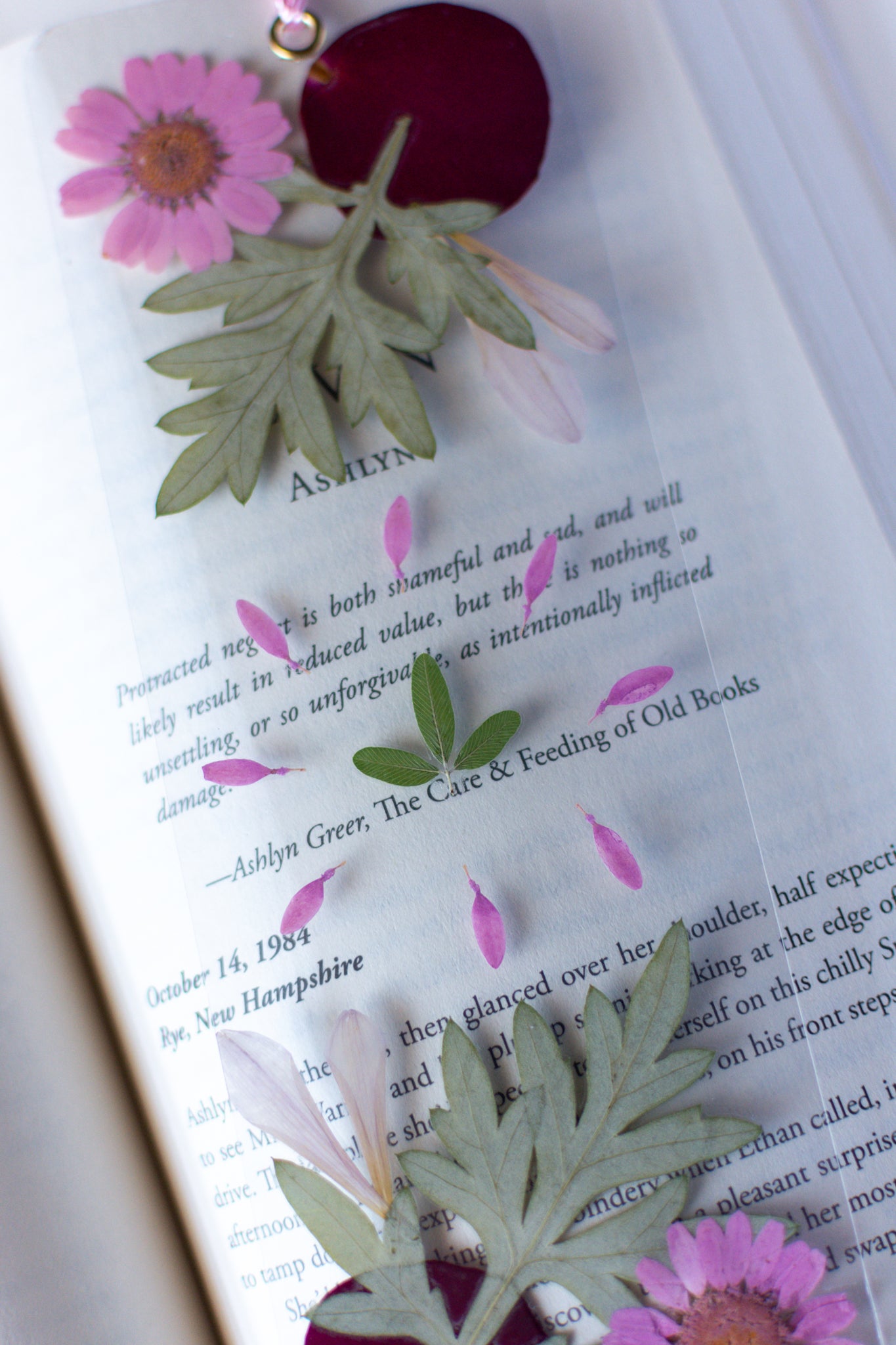 Un separador de libros transparente con flores prensadas en su interior de color rosa y verde.