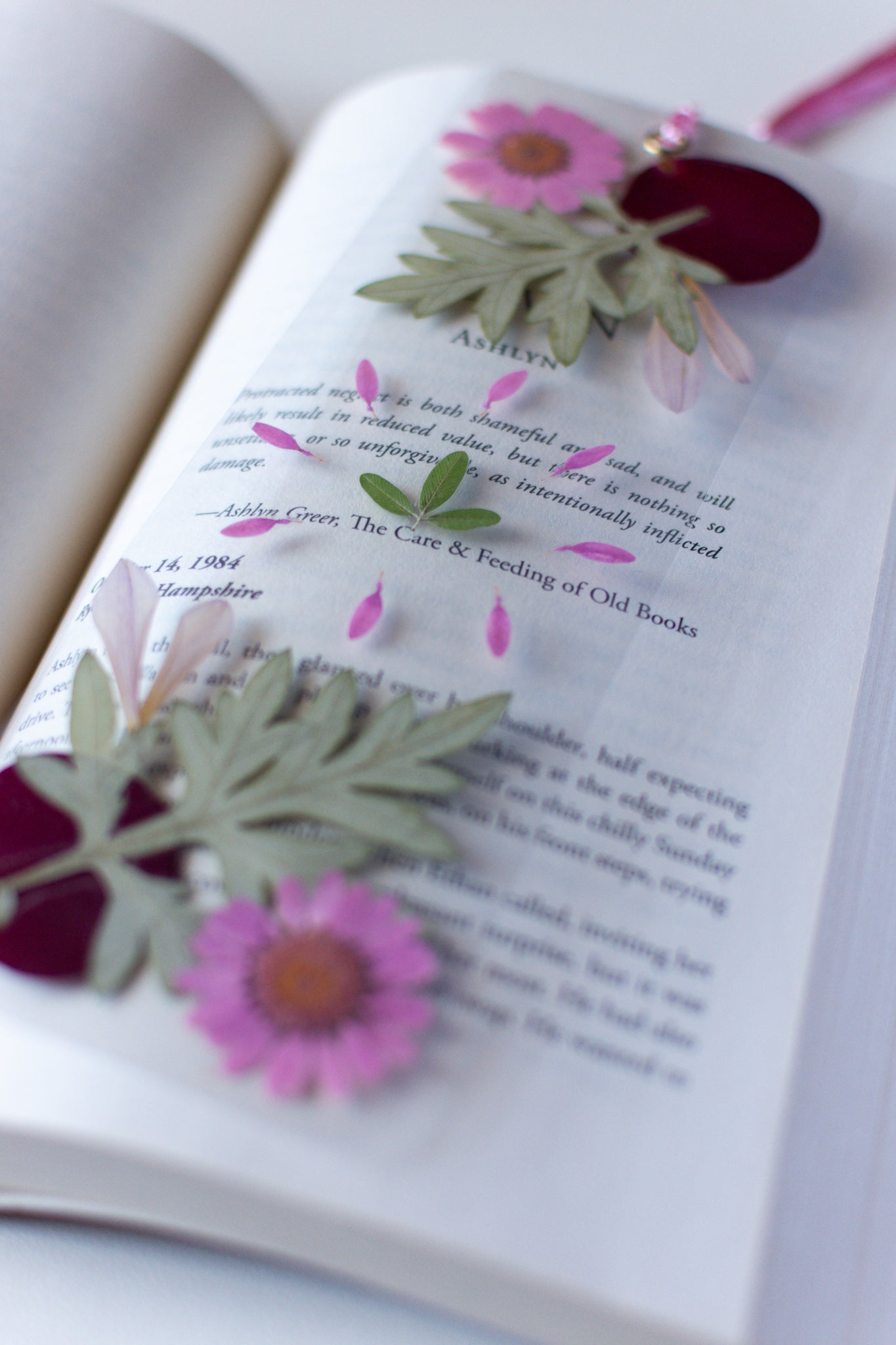 Un separador de libros transparente con flores prensadas en su interior de color rosa y verde.