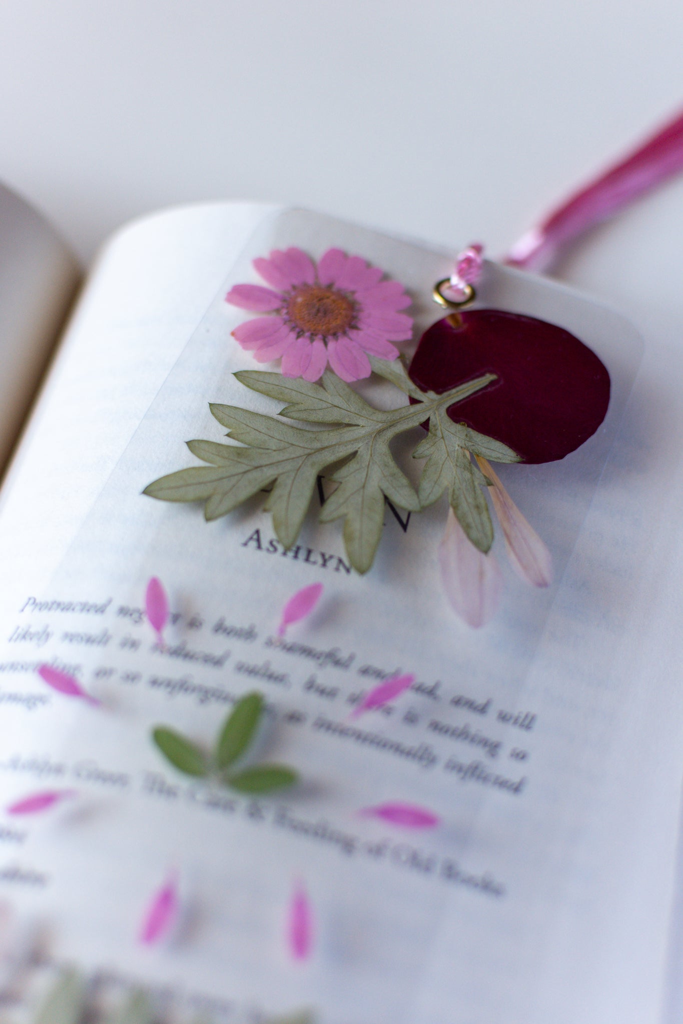 Un separador de libros transparente con flores prensadas en su interior de color rosa y verde.