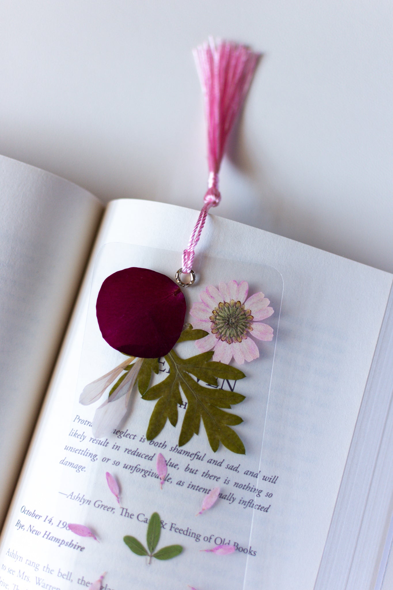 Un separador de libros transparente con flores prensadas en su interior de color rosa y verde.