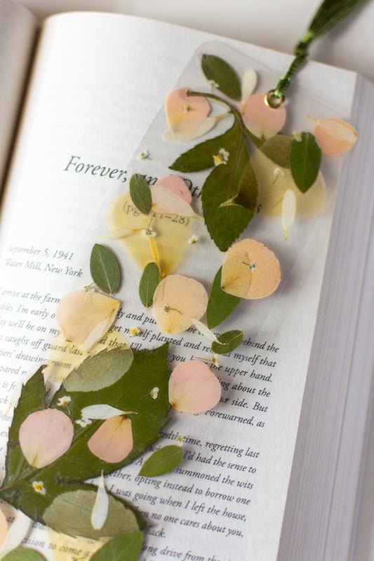 Un separador de libros transparente con pétalos prensadas en su interior de  color rosa y blanco. 