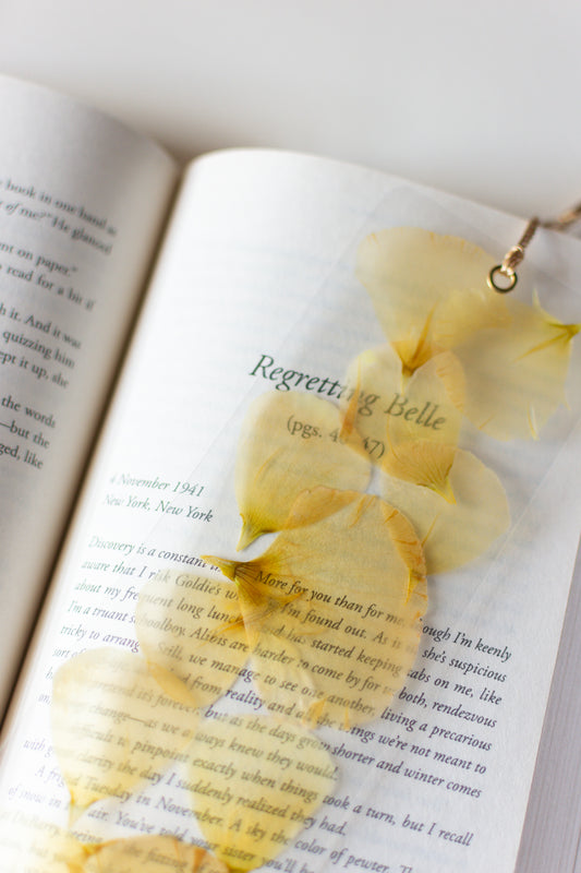 Separador de libros transparente con pétalos prensadas en su interior de color blanco.