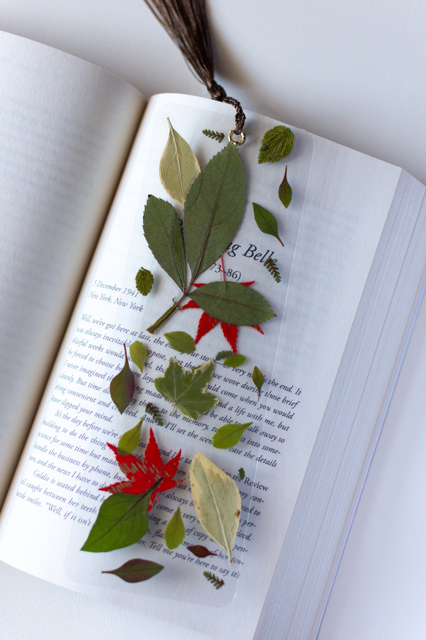 Un separador de libros transparente con hojas prensadas en su interior de color morado y blanco.